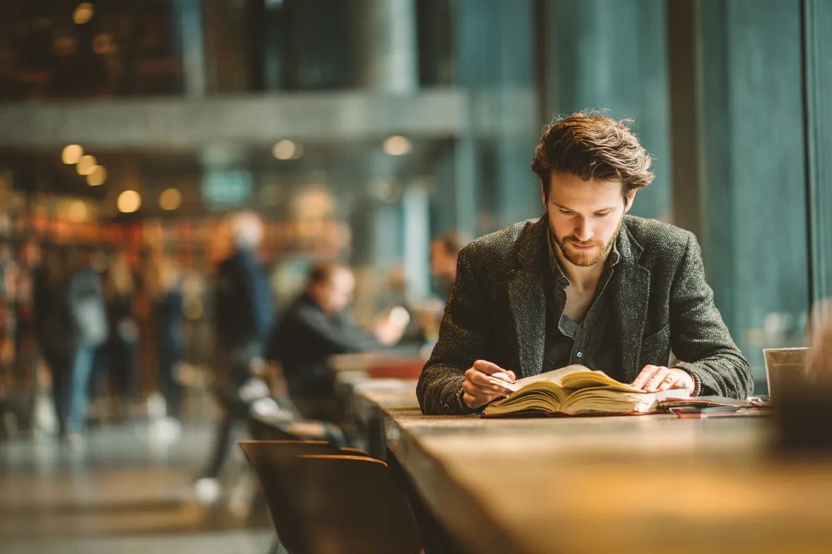 A man in his 30s studying a reference book at a long table in a modern public library, illustrating Personal Loan Glossary with Westside Lending